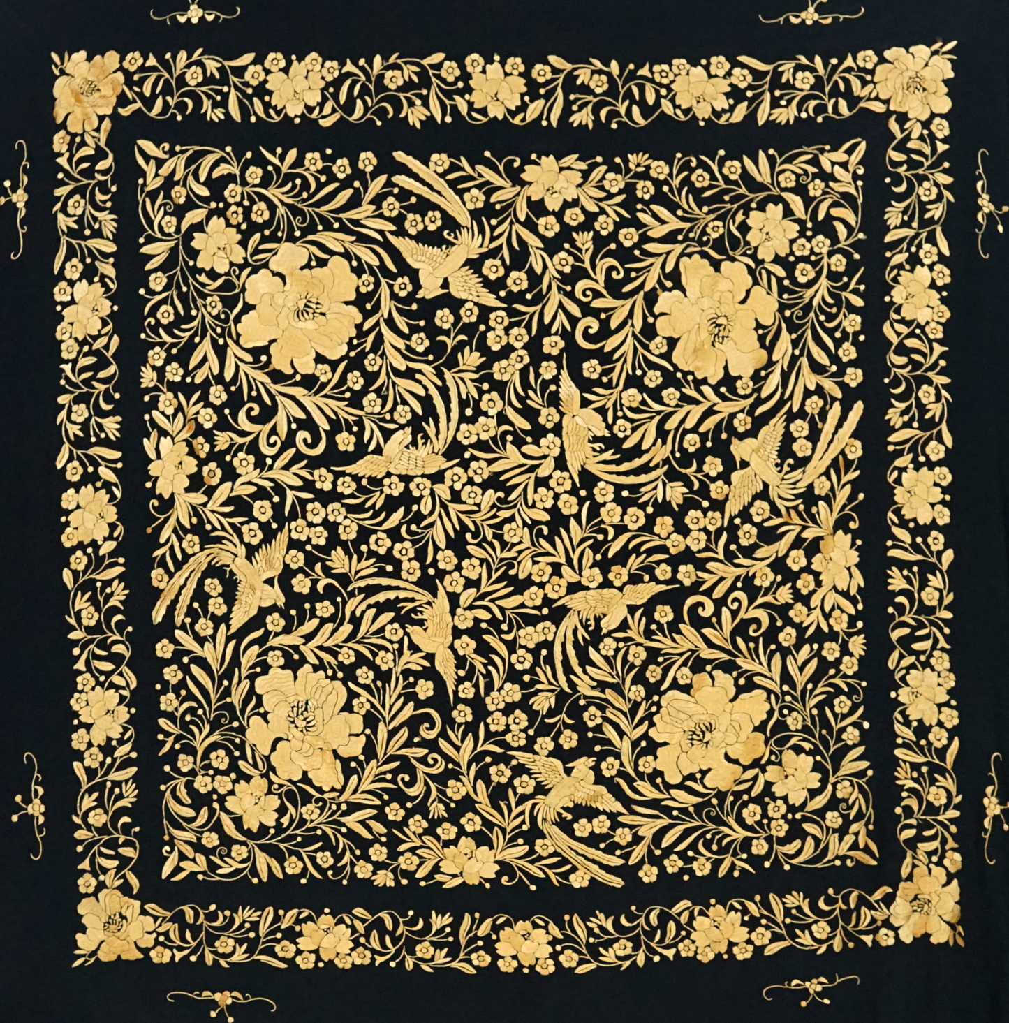 Mantón de seda natural bordado a mano. Pieza de 135 × 135 cm. Fondo negro con bordado en mostaza. Sofisticación cálida y moderna.