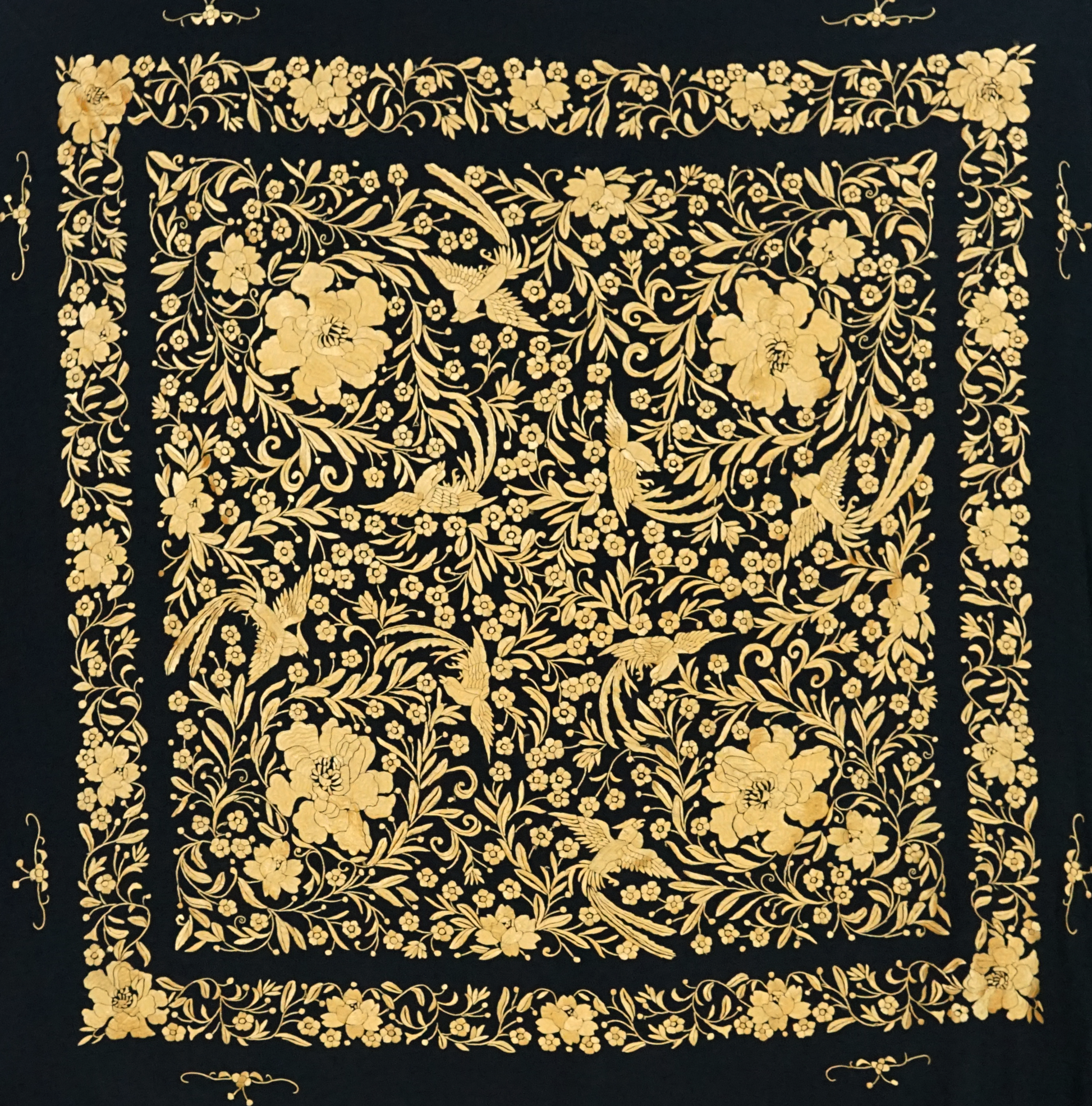 Mantón de seda natural bordado a mano. Pieza de 135 × 135 cm. Fondo negro con bordado en mostaza. Sofisticación cálida y moderna.